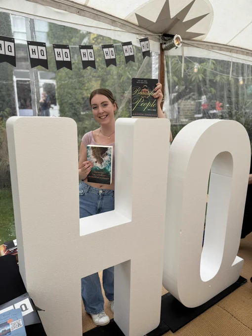 Caucasian female holding two books against large letters that are white spelling HQ