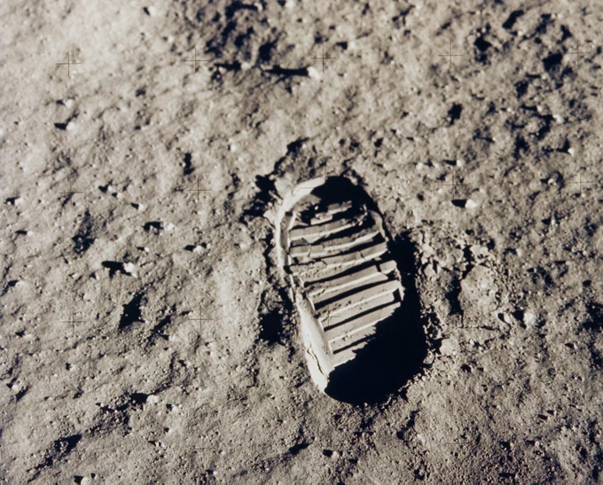 A bootprint on the Moon, made by American astronaut Buzz Aldrin during the Apollo 11 mission. The Moon's bumpy, gray surface stands out in sharp detail in this photo, as does the print, which is oval-shaped with thick lines running across its tread. 