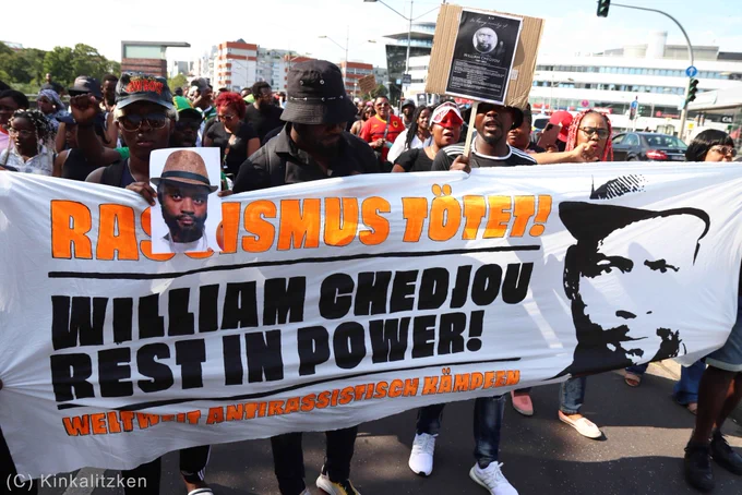 Banner: "Rassismus tötet! William Chedjou rest in power. Weltweit antirassistisch kämpfen".