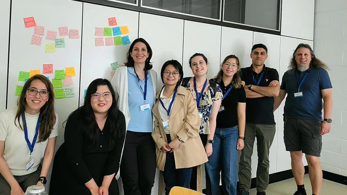 The attendees of the workshop standing in front of clustered summarizing sticky notes on the wall.