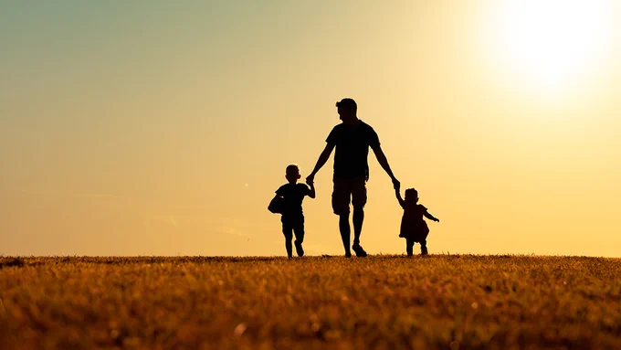 A father hold hands with his two young children.