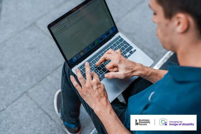 Close-up on the hands of someone with cerebral palsy as they use a laptop. The 'Changing the image of disability' logo is in the lower right corner of the image.