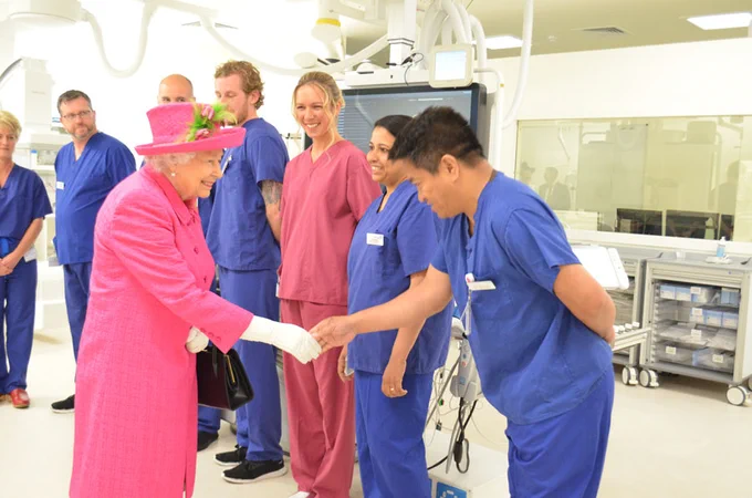 Queen Elizabeth II shakes hands with a nurse in blue scrubs in a cath lab