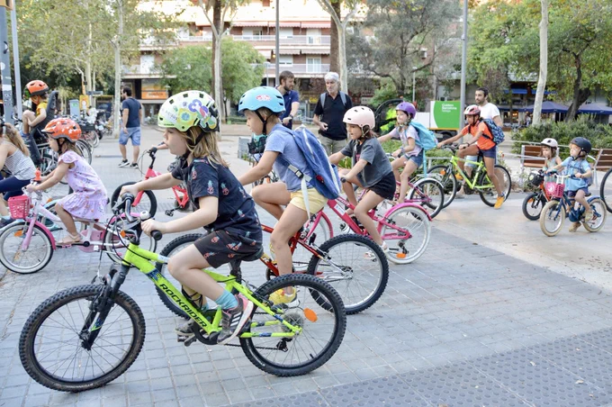 A group of 10 or so children cycle and scoot together in an organized “bike bus” on a street in Barcelona.