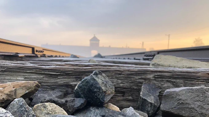 A contemporary view of the Gate of Death at the site of the former Auschwitz II-Birkenau. The gate is visible in the mist in the background. In the foreground, you can see the rails and stones of the rail line leading to the gate.