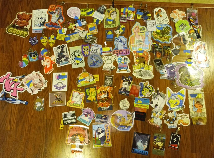 A picture of furry character badges of many types, species and sizes scattered on a wooden floor.