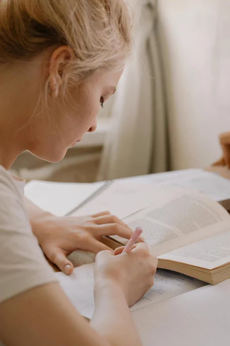 Picture of a person writing in a notebook with a book in front of them.