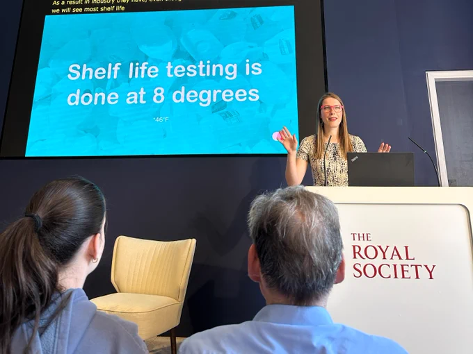 Solveiga presenting to an audience behind a lectern. The side reads: Shelf life testing is done at 8 degrees.