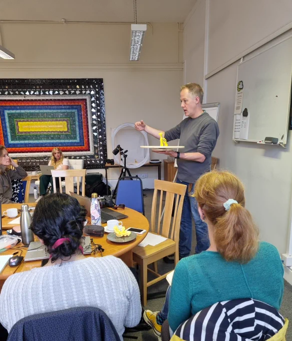 A Digital Humanities colleague holding up a duplo giraffe on a turntable to demonstrate photography techniques to workshop attendees.