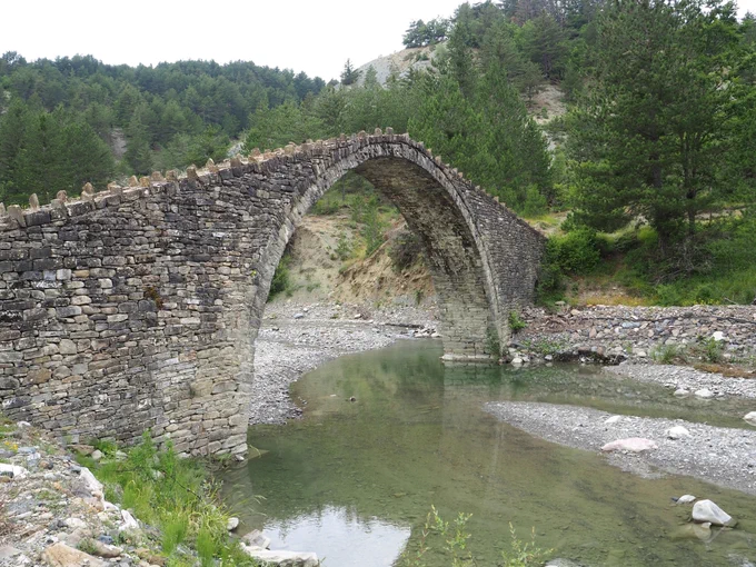 A stone arched bridge over a shallow stream.