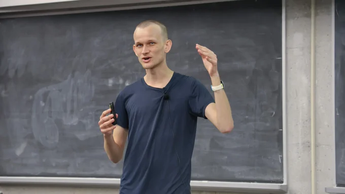 Vitalik Buterin talking at the front of a lecture hall with a blackboard behind him