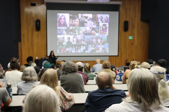 A full lecture hall looking at a speaker giving a presentation at the front.