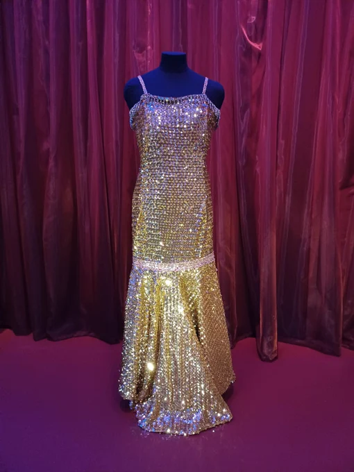 A shimmering gold dress on a red background, part of the Beyond the Bassline exhibition. 