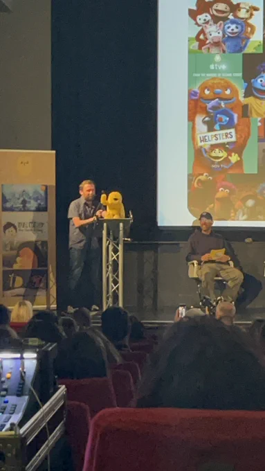 Puppeteer operates puppet on stage at the conference in front of a panel of judges