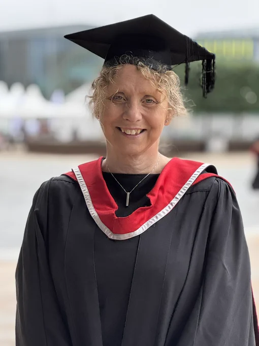 A graduate from Teesside University in black robe and red and grey hood.