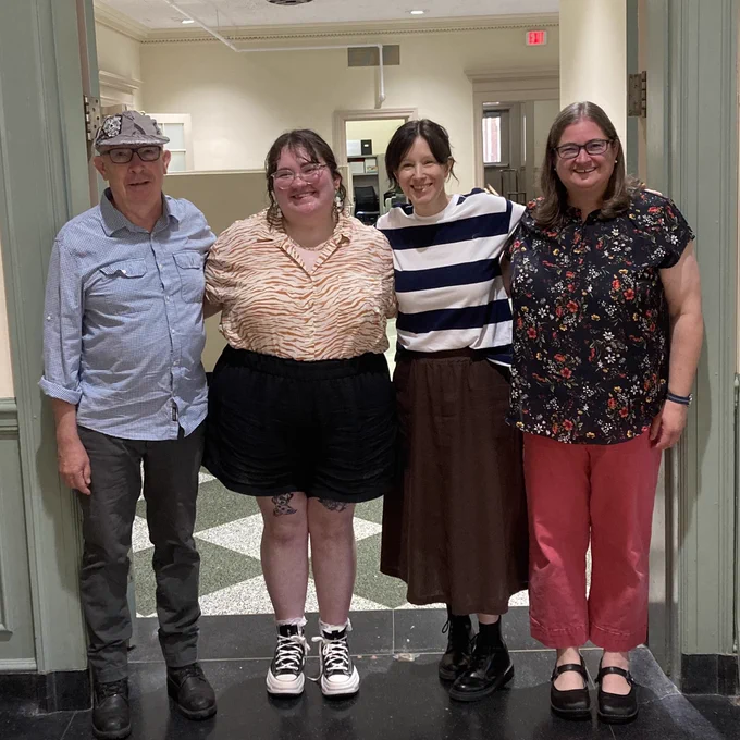 From left to right, Keith Tuma, Hallie Forgarty, Cathy Wagner, and Jen Sammons stand together smiling in Harris Hall. 