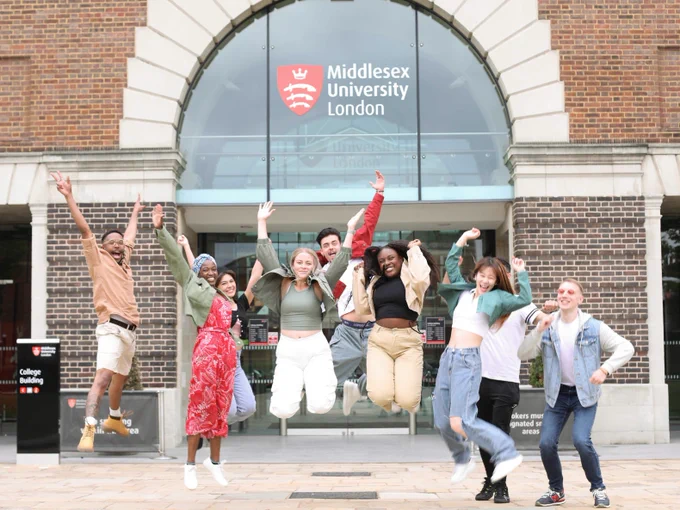 A group of joyful students jumping in front of Middlesex University London's main entrance.