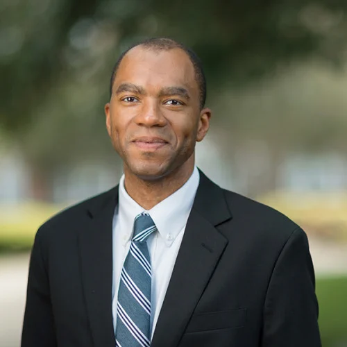 Photo of F Lee Francis, a man wearing a black suit, white shirt and blue striped tie. 