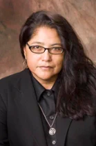 Photo of Guadalupe Luna, a woman wearing a black button down shirt with a black suit jacket. She is wearing glasses and has long black hair. 