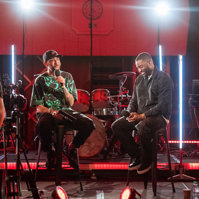 DJ Target and Bashy sit on stools in front of an audience at the exclusive BBC 1Xtra special and hold microphones. 