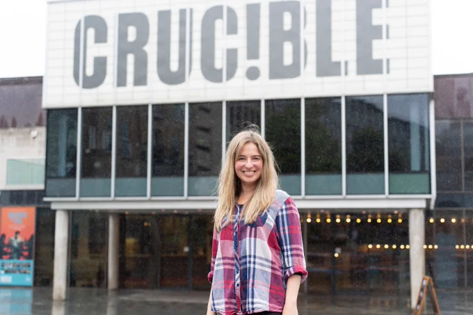 A woman wearing a red and blue shirt stands in front of the Crucible Theatre.