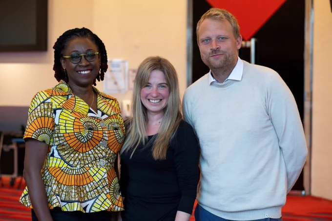 Three people stand close together and smile in a theatre foyer.