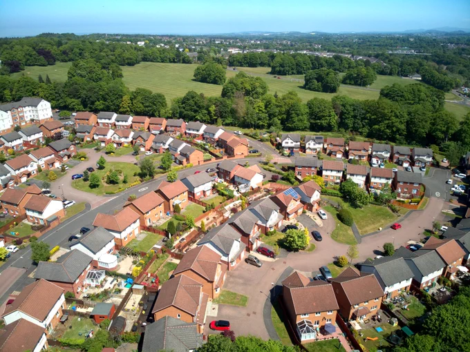 A cul de sac of houses on the edge of green fields and woodland (viewed from above)