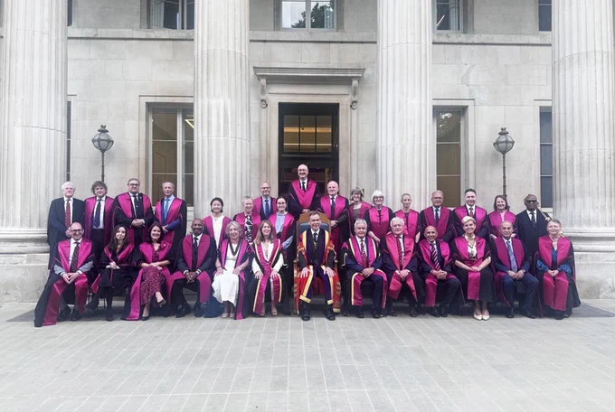 The RCS England Council pose for a photo on the steps of RCS England. They are wearing navy and red robes. 