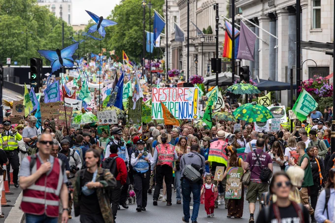 A large crowd walks on a march through London. They're holding banners and props including butterfly puppets