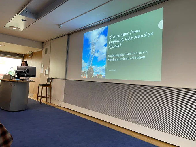 Lara, the trainee at the Law Library is standing behind a computer. The first slide of her presentation, entitled ''O Stranger from England why stand ye aghast' is projected onto the screen. 