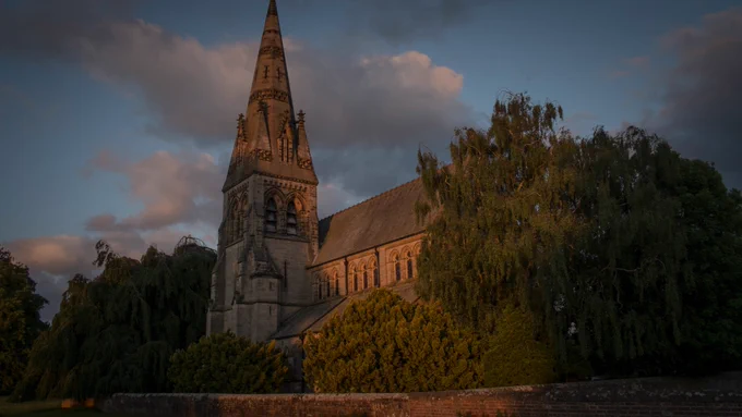 Photograph of Christ the Consoler an ornate Victorian church with a tall stone spire surrounded by willow trees at sunset (c) Graham White