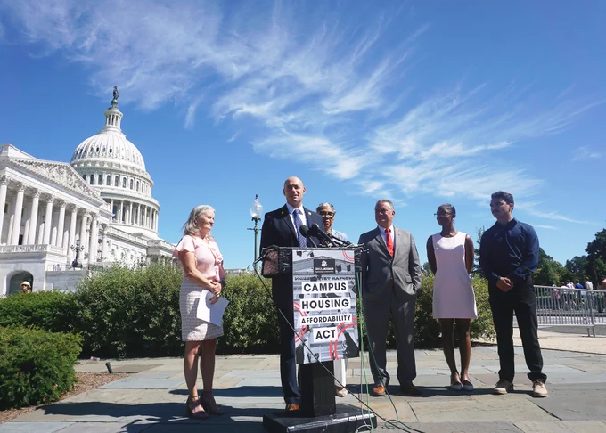 Rep. Greg Landsman standing at the podium and Capitol with other attendees. 