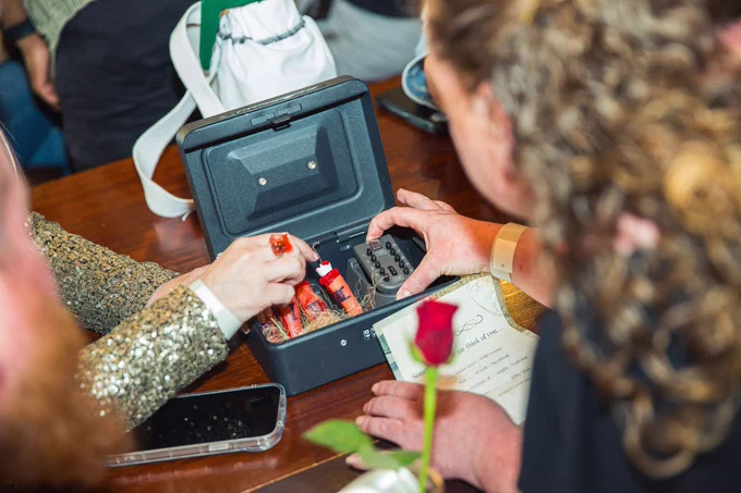 A person hands over cash payment to another, who is using a calculator within a briefcase, at a table with a visible document, smartphone, and a red rose.