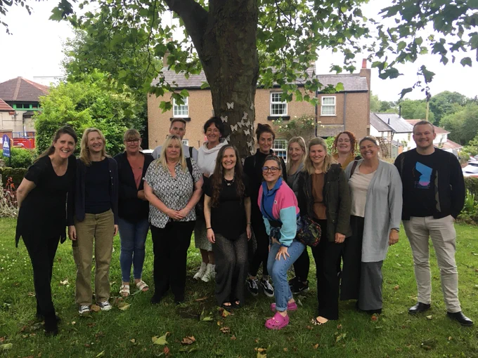 A group of fourteen smiling people beneath a tree