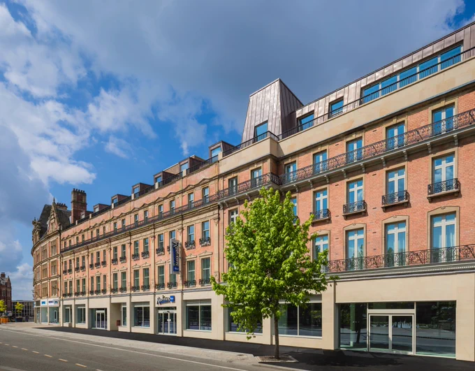 Picture shows an empty street with a tree in the foreground, behind the tree and spreading across the picture is the new Radisson Blu hotel in Sheffield.