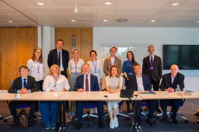 Secretary of State Steve Reed and Baroness Hayman pictured with leaders from 11 environmental NGOs. The Secretary of State and Baroness are seated behind tables with four of the leaders. Seven of the leaders are stood behind those who are seated. They are in a well-lit office space and everyone is smiling at the camera.