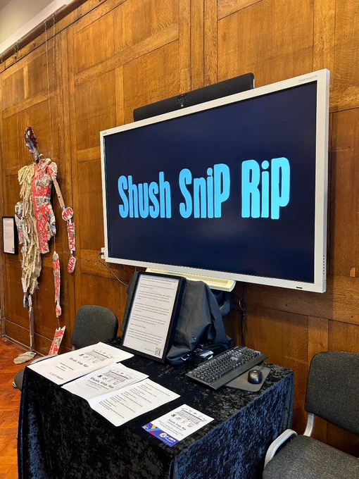 A screen with the words 'Shush Snip Rip' on. Next to the screen is a large puppet-like sculpture.