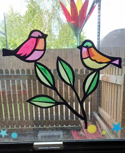 A stained glass effect design made from tissue paper that shows birds and leaves 