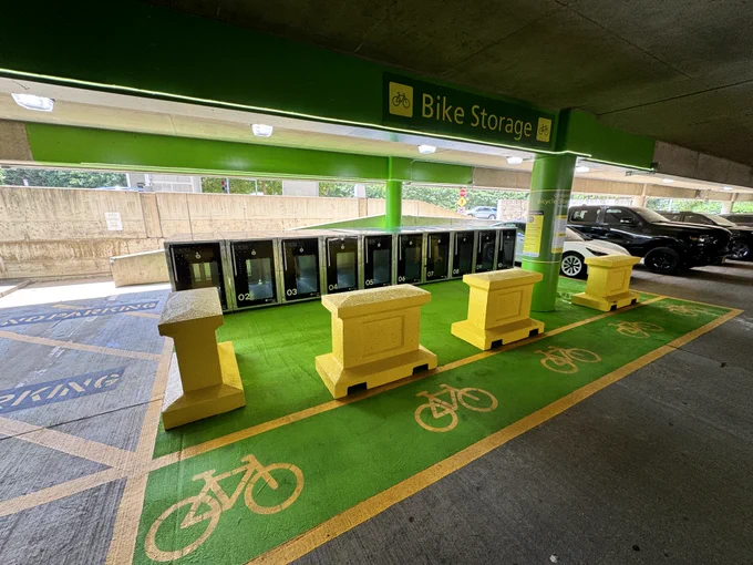 Row of black bike lockers located in a well-lit parking garage with designated green bike lanes, marked with "Bike Storage" signage at Reagan National Airport