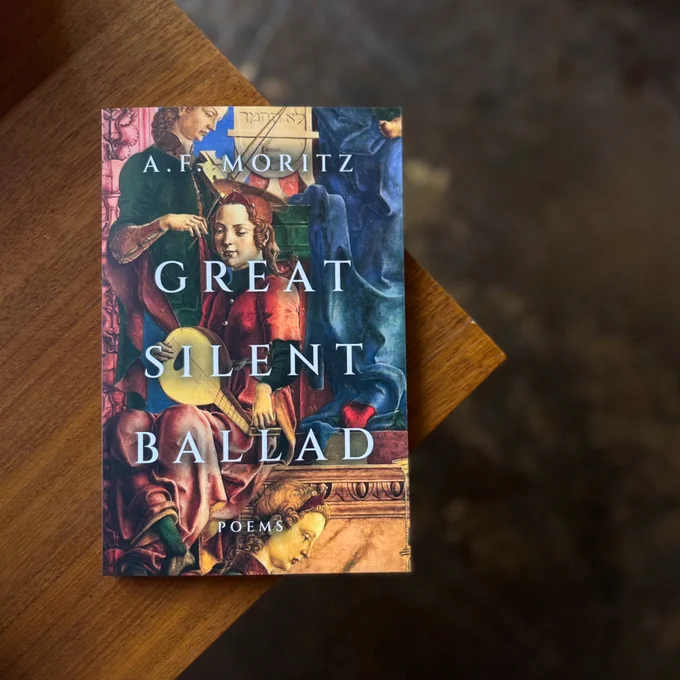 A photo of the book Great Silent Ballad on the edge of a wooden table. The photo is taken from above. 