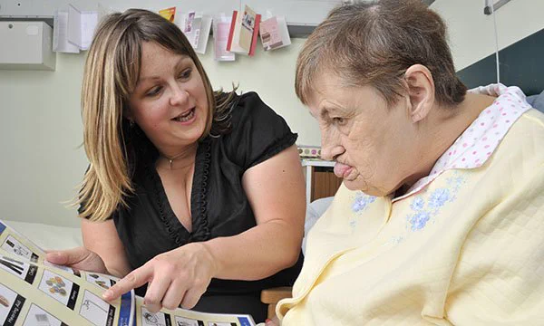 Woman with a learning disability sitting up in a hospital bed being shown an easy read leaflet.