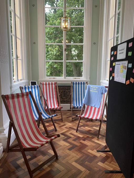 A display of red and white deck chairs and blue and white striped deck chairs in a large bay window. 