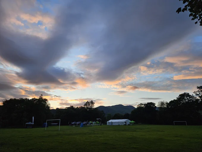 View of Rothay Park with marquee. Fells outlined in sky where the evening sun is catching the grey clouds with tinge of pink.