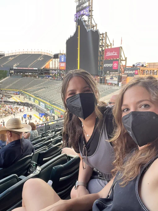 Two white brunette females wearing black respirators sitting at Coors Field in Denver.