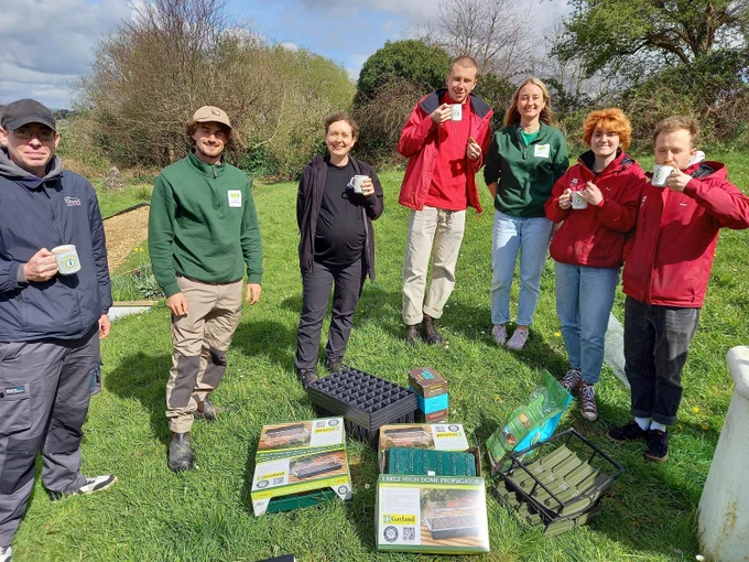 Group of people standing around plant propagators, holding cups of tea