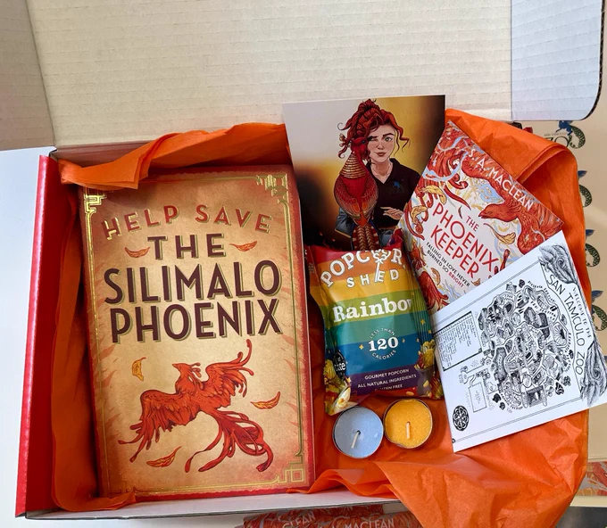 A box including The Phoenix Keeper proof, a packet of rainbow popcorn, one blue tealight, one orange tealight, one character postcard, one zoo map postcard and orange tissue paper