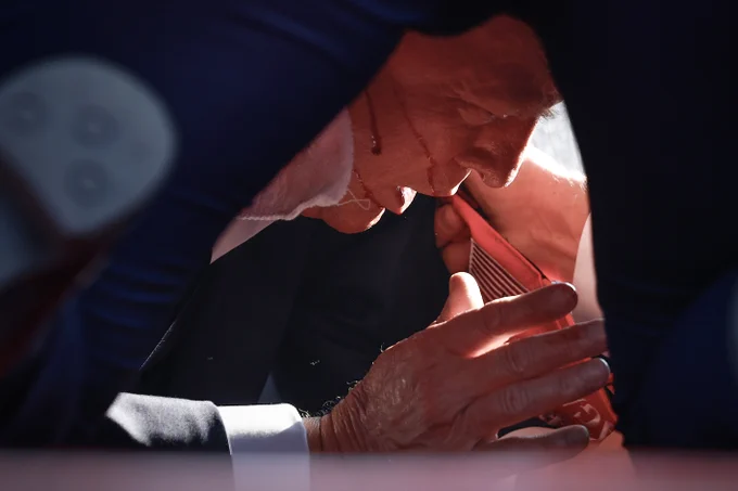 Trump covered by Secret Service agents, with blood lines running across his face.