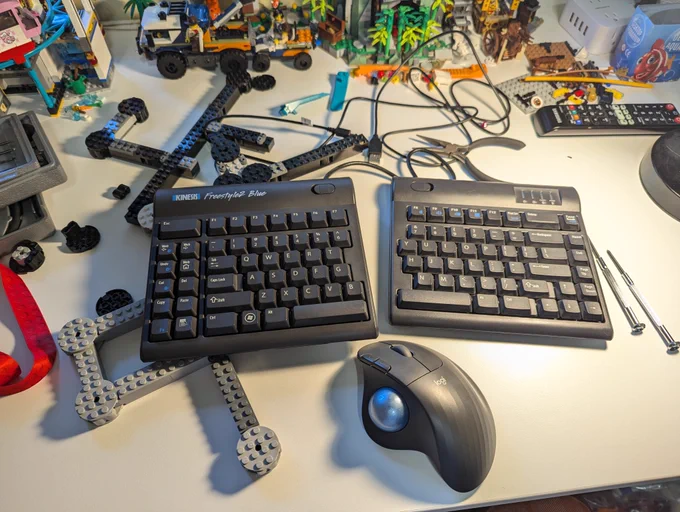 Workbench with split computer keyboard, trackball mouse, various LEGO, and small screw drivers.