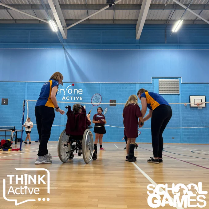 Image shows four students having help to play badminton from voulenteers above the School Games and Think Active logos