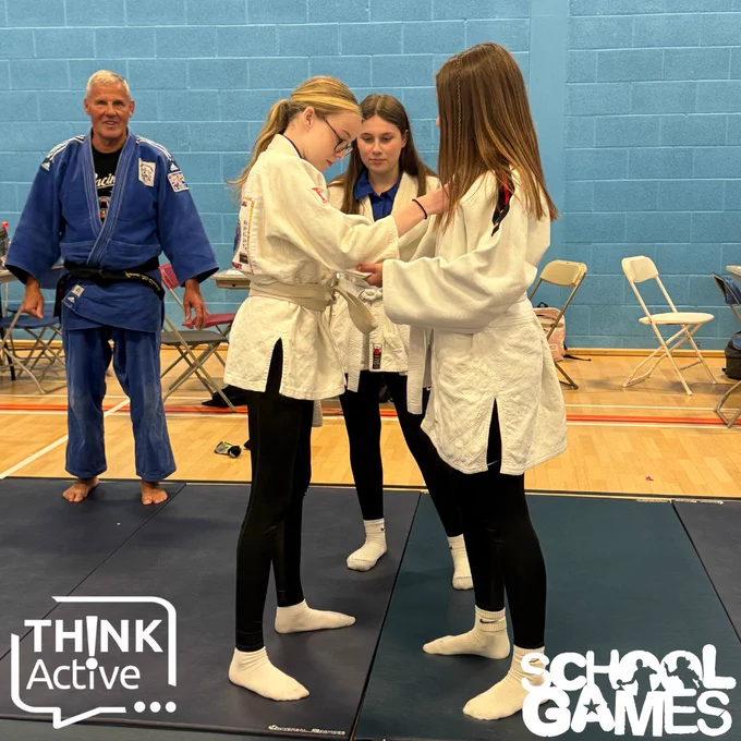 Image shows three girls learning judo from their instructor above the School Games and Think Active logos